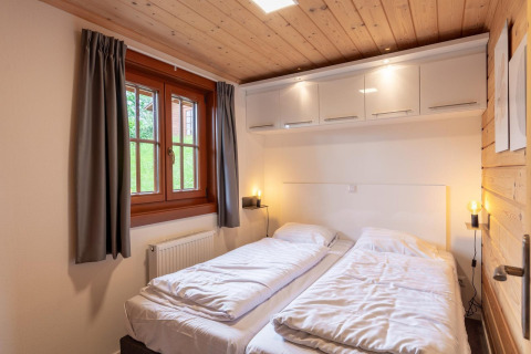 Dormitorio con camas individuales, techo de madera, ventana y armarios en Boekhorst lodge, Brunssummerheide, Países Bajos.