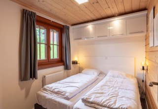 Camera da letto con due letti singoli, soffitto in legno, finestra e armadi nel lodge Boekhorst, Brunssummerheide, Paesi Bassi.