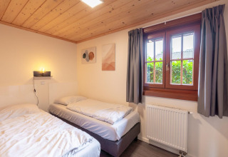 Knusse kamer met twee eenpersoonsbedden, houten plafond en raam in Boekhorst Lodge op Brunssummerheide.
