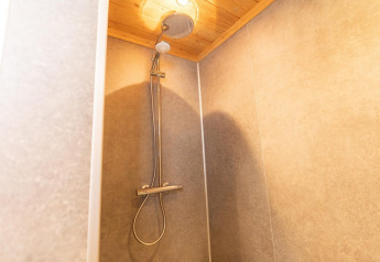 Moderne douche in de Boekhorst-lodge bij Brunssummerheide, Nederland, met houten plafond en lichte tegels.