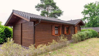 Buitenaanzicht van Boekhorst Royal lodge met houten gevel, groene struiken en een grasveld overdag.