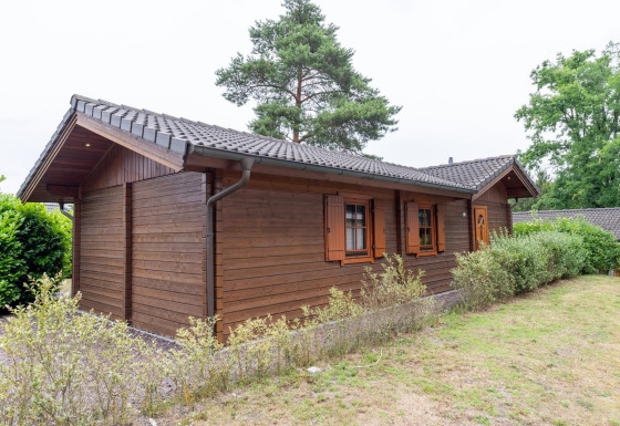Buitenfoto van het Boekhorst Royal lodge met houten wanden, groene struiken en gazon in daglicht.