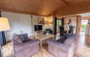Stue i Boekhorst Royal lodge ved Brunssummerheide, Nederland, med træloft, sofaer og spisebord.