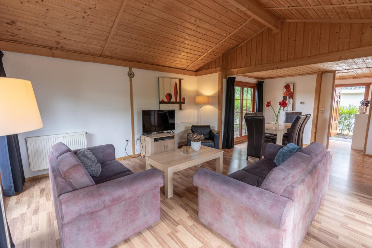 Sala de Boekhorst Royal lodge en Brunssummerheide, Países Bajos, con sofás, comedor y techo de madera.
