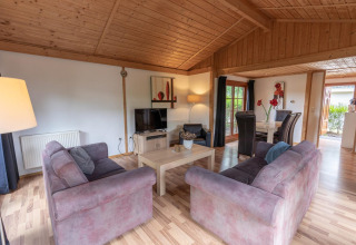 Sala de Boekhorst Royal lodge en Brunssummerheide, Países Bajos, con sofás, comedor y techo de madera.