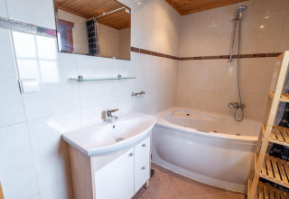 Salle de bain moderne avec lavabo blanc, miroir, baignoire d’angle et étagère à Boekhorst Royal, Brunssummerheide.