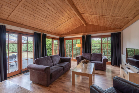 Salon du lodge Boekhorst Royal à Brunssummerheide, Pays-Bas, avec plafond en bois, grandes fenêtres et canapés.