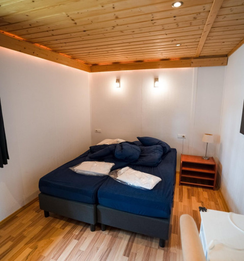 Dormitorio con cama doble, sábanas azules, techo de madera y lámparas en Boekhorst Royal, Brunssummerheide.