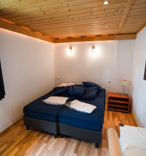 Dormitorio con cama doble, sábanas azules, techo de madera y lámparas en Boekhorst Royal, Brunssummerheide.