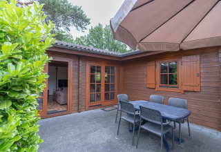 Patio esterno al Boekhorst Royal lodge, Brunssummerheide, Paesi Bassi, con tavolo, sedie e ombrellone.
