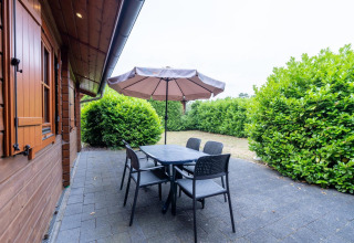 Patio esterno al Boekhorst Royal lodge a Brunssummerheide, Paesi Bassi, con tavolo, sedie e ombrellone.