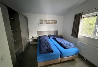 Kamer met twee eenpersoonsbedden, blauwe lakens en donkere dekbedden in L-Pavilion, Brunssummerheide.