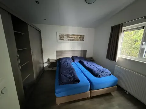 Habitación con dos camas individuales, sábanas azules y edredones oscuros en L-Pavilion, Brunssummerheide.