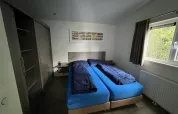 Zimmer mit zwei Einzelbetten, blauer Bettwäsche und dunklen Decken im L-Pavilion bei Brunssummerheide.