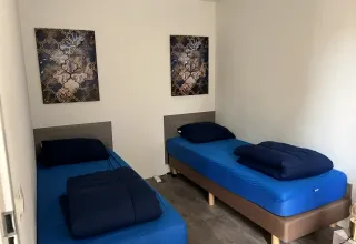 Twee eenpersoonsbedden met blauw beddengoed en wandkunst in een kamer bij L-Pavilion, Brunssummerheide, Nederland.