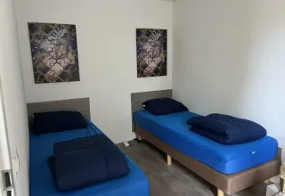 Twee aparte bedden met blauwe lakens en wanddecoratie in een kamer van L-Pavilion, Brunssummerheide, Nederland.