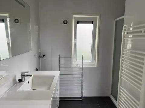 Moderne badkamer in L-Pavilion, Brunssummerheide, Nederland, met grote wastafel en raam.