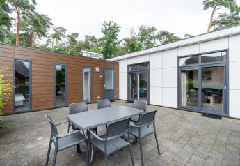 Udendørs terrasse ved L-Pavilion på Brunssummerheide i Holland med spisebord og stole foran en moderne lodge.