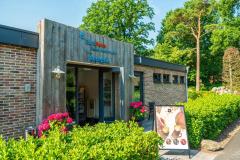 Reception building at a glamping resort with flowers and a sign, surrounded by lush greenery and trees.