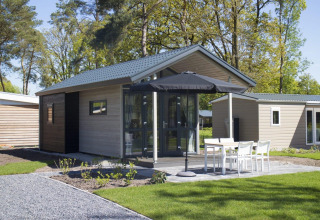 Moderne tiny house aan Reestervallei in Nederland, met terras, tuinset en grote zwarte parasol.