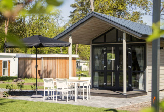 Modern tiny house at Reestervallei in the Netherlands, featuring patio seating and a black umbrella.