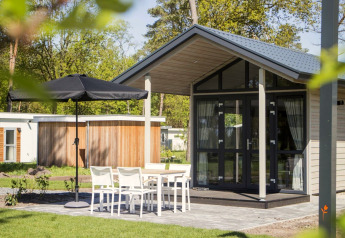 Tiny House moderna a Reestervallei nei Paesi Bassi con tavolo all’aperto, sedie bianche e ombrellone nero.