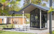 Modern tiny house at Reestervallei in the Netherlands, featuring patio seating and a black umbrella.