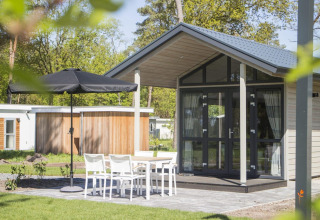 Moderna Tiny House en Reestervallei, Países Bajos, con mesa exterior, sillas blancas y sombrilla negra.