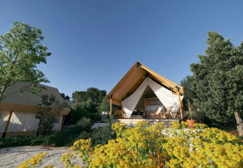 Glampingtent lodge con tende di lusso circondate da alberi e fiori, sotto un limpido cielo azzurro.
