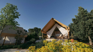 Glampingtent-Lodge mit Zelt, eingebettet in grüner Natur mit Blumen und Bäumen unter klarem Himmel.