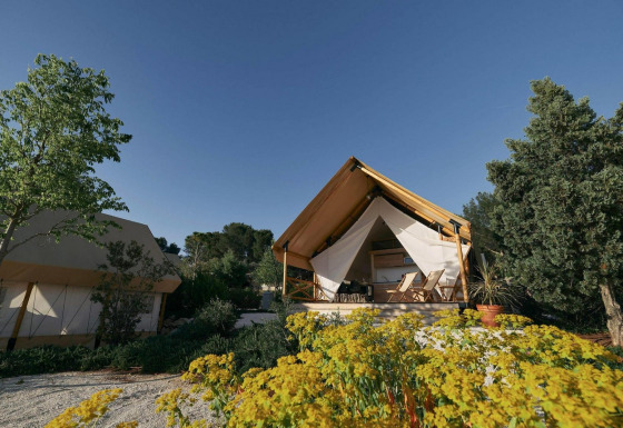 Glampingtent lodge con tende di lusso circondate da alberi e fiori, sotto un limpido cielo azzurro.