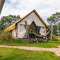 Glampingtent met hangmat en picknicktafel buiten, omgeven door gras en bomen op een camping.