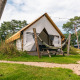 Glamping tent with hammock and picnic table outside, surrounded by grass and trees at a campsite.