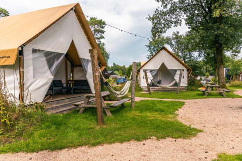 Tienda de glamping en Reestervallei, Países Bajos, con terraza, hamaca y mesas de picnic exteriores.