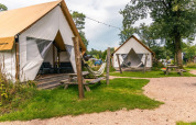 Glamping tent at Reestervallei in the Netherlands, with deck, hammock, picnic tables and green lawn.