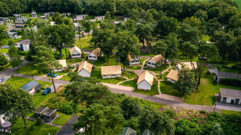 Aerial view of glamping tents and lodges at Reestervallei in the Netherlands, nestled within green woods.
