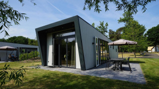 Moderne Just Nature-Lodge mit großer Terrasse und Sitzbereich im Freien in grüner Umgebung.