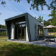 Moderne Just Nature-lodge med stor terrasse og udendørs siddeplads i grønne omgivelser.