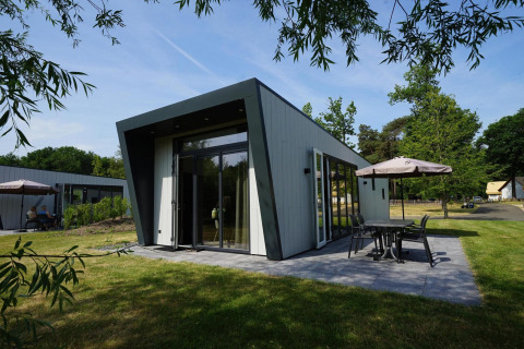 Moderne Just Nature-lodge met een ruim terras en tuinmeubelen, omringd door groen landschap.