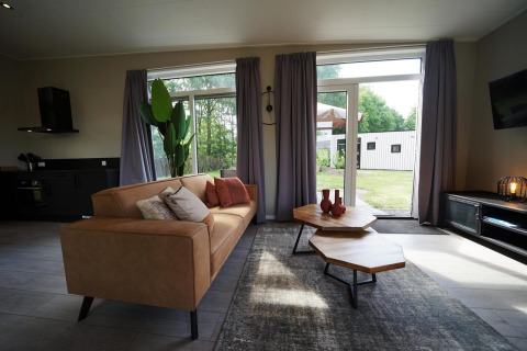 Salon moderne d'un lodge à Just Nature, Reestervallei, Pays-Bas, avec grandes fenêtres et décor élégant.