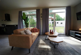 Salon moderne d'un lodge à Just Nature, Reestervallei, Pays-Bas, avec grandes fenêtres et décor élégant.