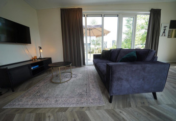 Moderne stue i Just Nature Lodge på Reestervallei, Nederlandene, med stor sofa og glasvinduer.