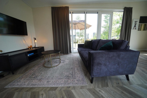 Moderne woonkamer in Just Nature Lodge te Reestervallei, Nederland, met sofa en grote ramen.