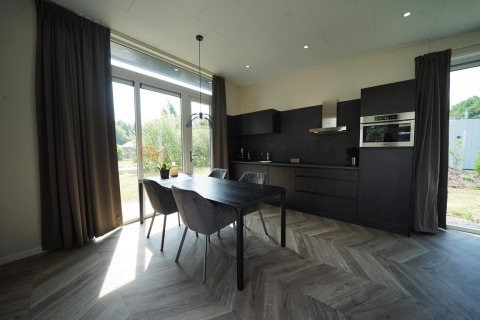 Cuisine moderne et salle à manger au lodge Just Nature de Reestervallei, Pays-Bas, avec grandes fenêtres et déco sombre.