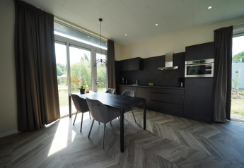 Moderne lodgekøkken ved Just Nature Reestervallei med sort interiør, spisebord og store vinduer til haven.