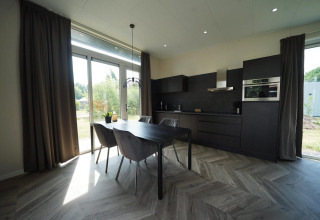 Moderne keuken en eetruimte in de Just Nature lodge in Reestervallei, Nederland, met grote ramen en donkere stijl.