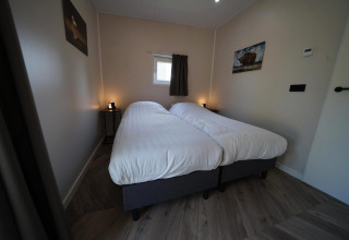 Moderne slaapkamer in de Just Nature-lodge in Reestervallei, Nederland, met twee enkele bedden en eenvoudige inrichting.