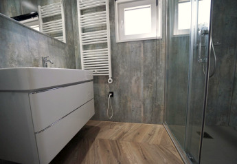 Modernes Badezimmer mit Glasdusche, Holzoptikboden, Wandwaschbecken und Handtuchheizkörper, Reestervallei.
