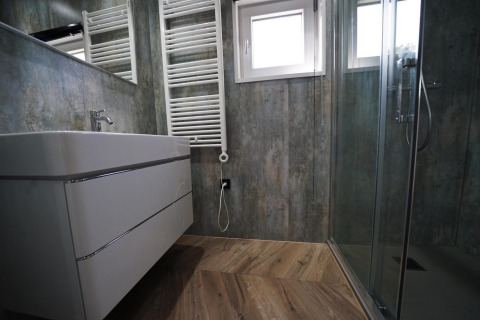 Baño moderno con ducha de cristal, suelo de madera, lavabo flotante y radiador toallero en Reestervallei.