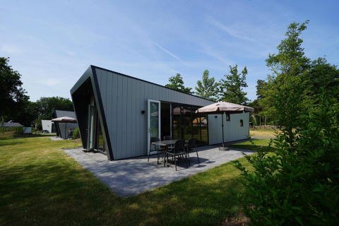 Un lodge moderno de Just Nature en Reestervallei, Países Bajos, con patio, mesa y sombrilla en el jardín.